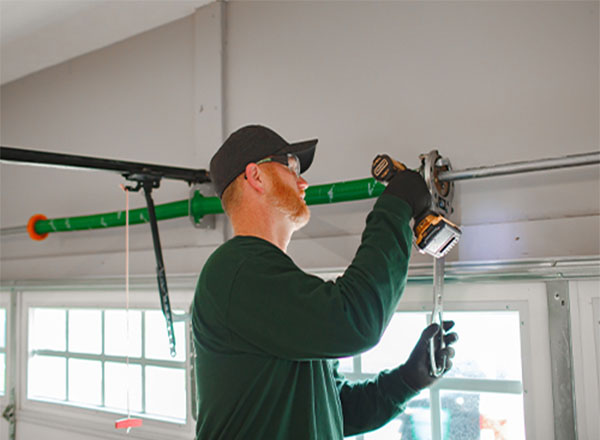 A technician adjusting a garage door system using a drill and wrench, ensuring balanced door operation for smooth and efficient movement.
