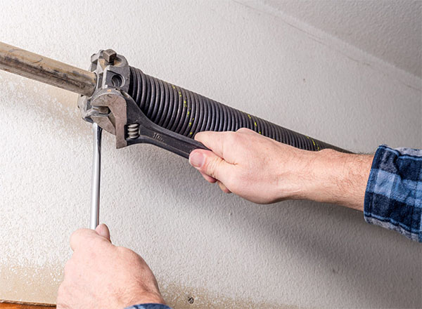 Technician using a wrench and a winding bar to safely replace a broken garage door spring.