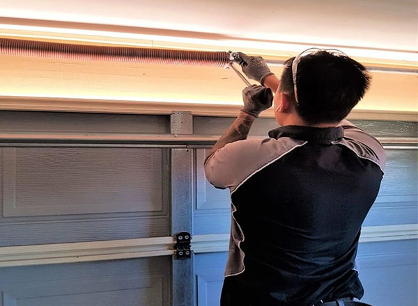 Technician installing a custom torsion spring on a residential garage door system.