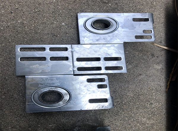 A set of metal end brackets with multiple slots and an oval cutout, designed for securing garage door components.