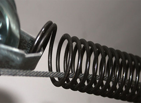 A close-up view of a garage door extension spring connected to a cable, highlighting the tension and proper alignment needed for smooth door operation.