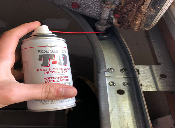 Applying rust-prevention lubricant to a garage door track and hardware to protect against corrosion and ensure smooth operation.