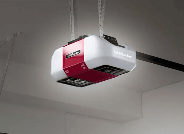 A LiftMaster garage door opener is shown mounted to a garage ceiling. The opener is primarily white and red.
