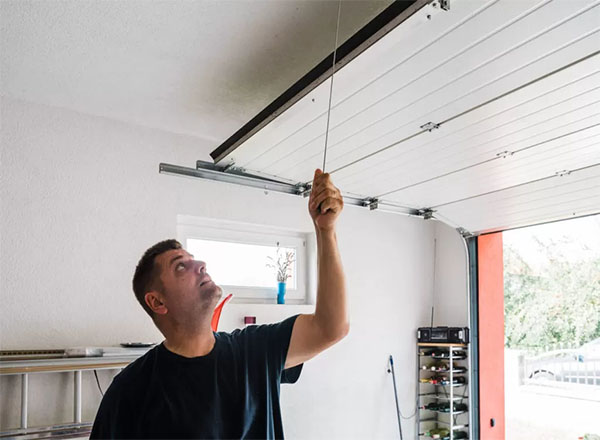A homeowner performing a safety check on a garage door by manually pulling the emergency release cord to ensure proper functionality. A homeowner performing a safety check on a garage door by manually pulling the emergency release cord to ensure proper functionality. A homeowner performing a safety check on a garage door by manually pulling the emergency release cord to ensure proper functionality.
