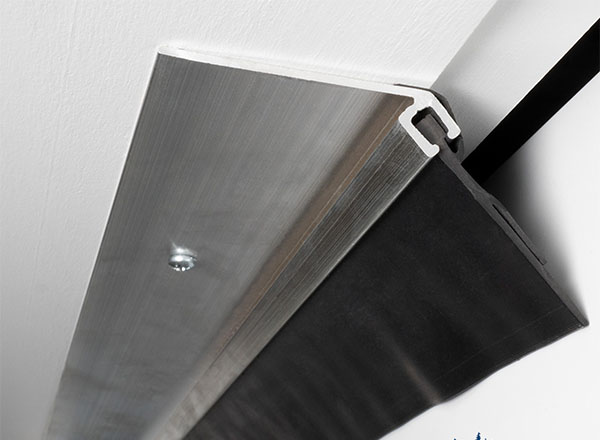 A close-up view of a garage door side and top weatherstripping with an aluminum retainer and a black rubber seal for insulation and weather protection.