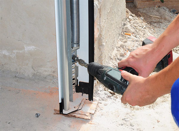 Technician using a power drill to adjust a vertical garage door spring mechanism. Technician using a power drill to adjust a vertical garage door spring mechanism. Technician using a power drill to adjust a vertical garage door spring mechanism.