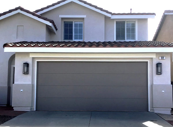A gray garage door on a light-colored stucco house with a red tile roof.
