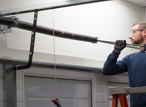 A technician wearing safety glasses and gloves carefully adjusting a torsion spring on a garage door system to ensure proper balance and smooth operation.