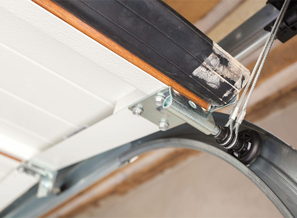 Garage door track and roller system with a metal bracket and cable attached to the bottom section.