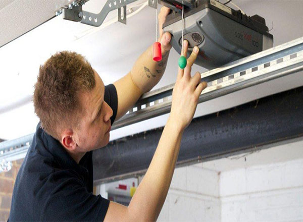 A technician performing a visual inspection of a garage door opener, checking its components for issues such as loose wiring or misalignment.