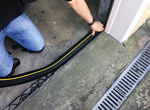 Installing a black garage door weather seal with a yellow stripe to prevent drafts, water, and debris.